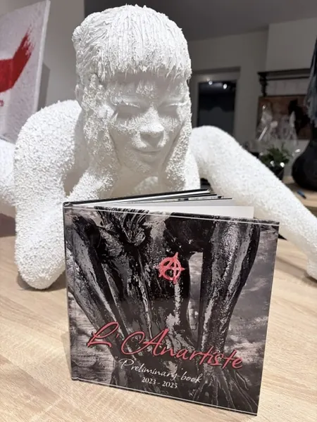 Sculpture blanche d’une femme accoudée, posée sur un catalogue de l’artiste